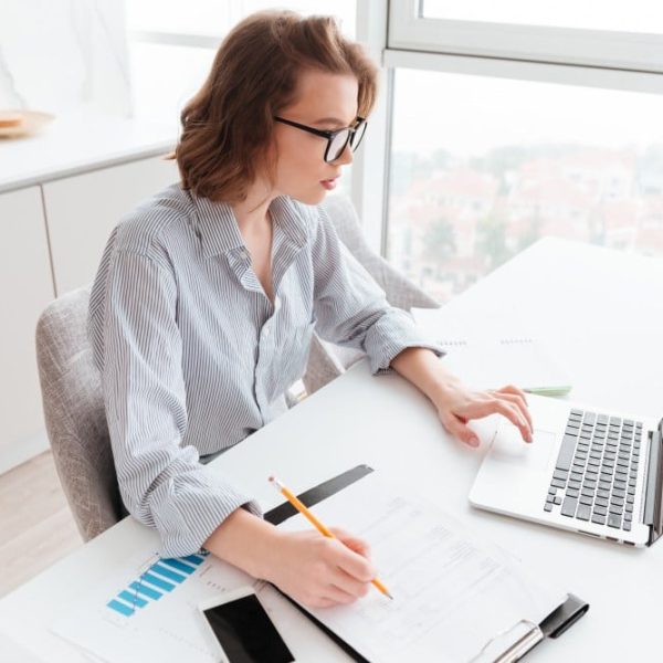 Femme travaillant sur ordinateur portable avec des documents dans un bureau lumineux